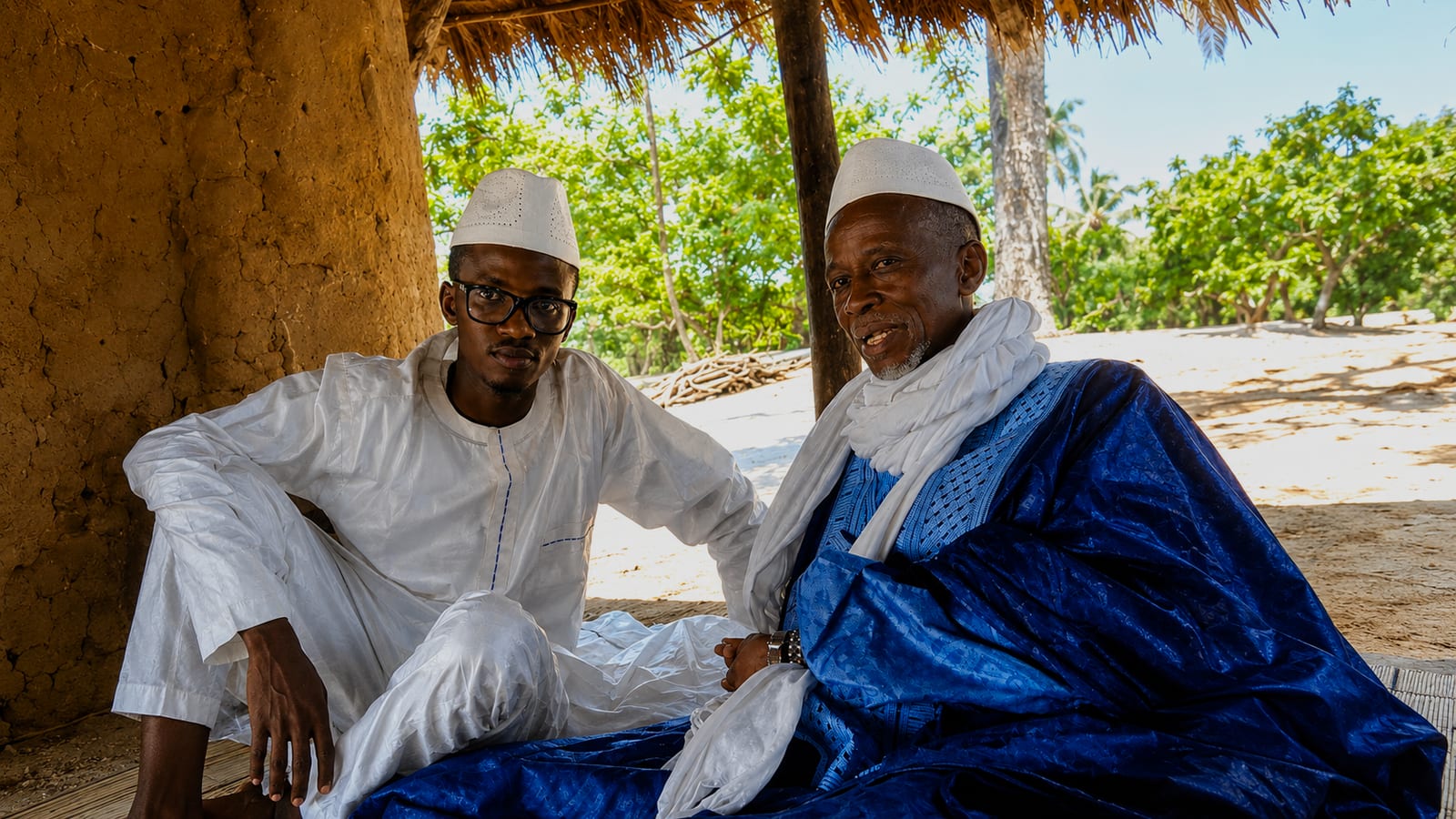 Entretien traditionnel sous un abri de paille, en boubou blanc et bleu